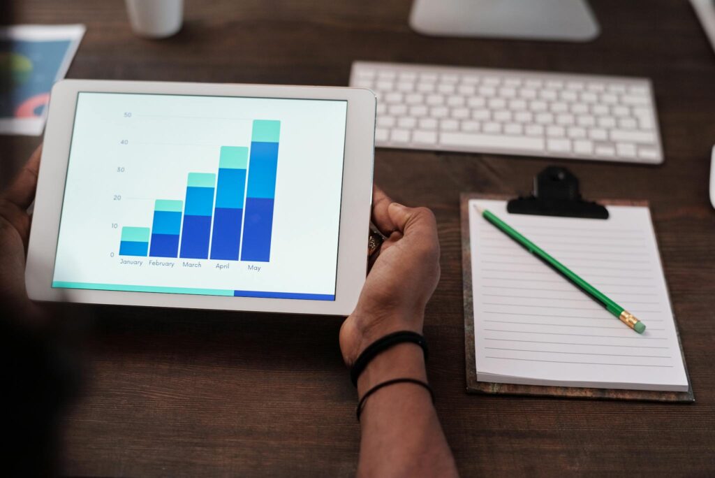 Close-up of a person holding a tablet showing growth charts on a wooden desk setup.